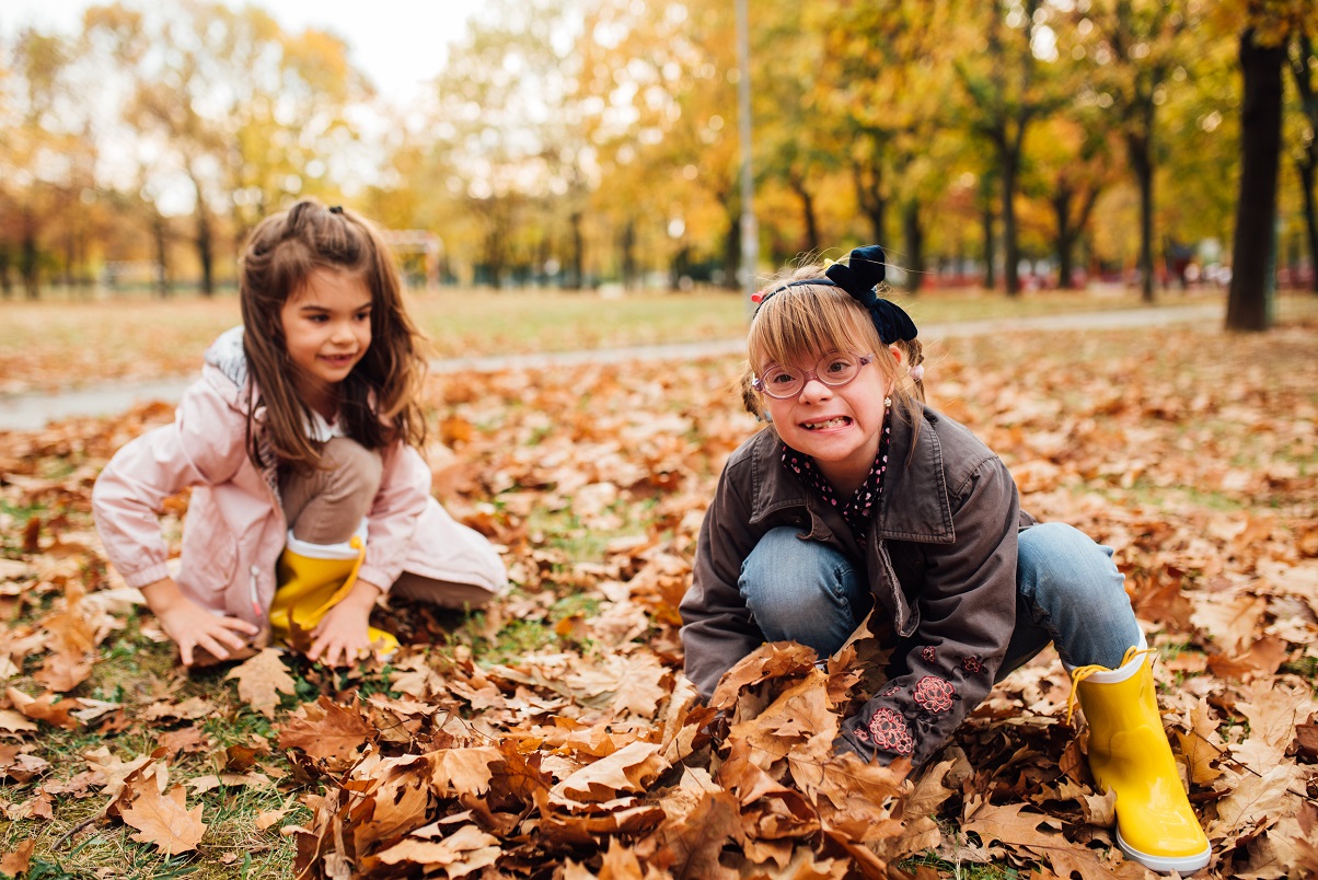 Little girl with Down syndrome and her best friend having fun with the autumn leaves.